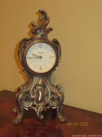 Front view of the vintage Mercedes West Germany mantel clock showing the ornate metal case and white clock face with numerals.