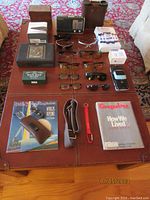 Wide overhead view of all items laid out on a table, showing multiple pairs of glasses, books, magazines, personal care items, and electronic devices.