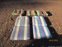 Four outdoor pillows placed on ground - two rectangular chair cushions and two other cushions with multi-colored vertical stripes in green, red, and black