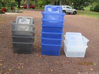 Photo showing three stacks of plastic storage containers in translucent black, blue, and clear colors arranged outdoors.