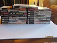 Stack of 17 PlayStation 2 games showing titles including Tony Hawk's Underground, NCAA Football, NBA Live, Madden, and more.
