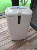Front view of white Rollibot portable air conditioner with digital display control panel, placed on a wood floor near a window.