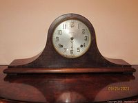 Front view of vintage Sessions mantel clock showing wood case, curved top, round silver-tone dial with Arabic numbers and black hands under glass with brass edge.
