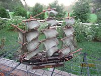 Full view of the vintage sailing ship model showing three masts with sails, hull, and rigging outdoors on a metal stand.