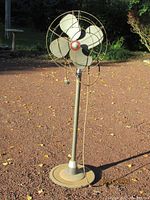 Front view of vintage Westinghouse industrial oscillating floor fan with four metal blades, metal cage, and circular base on gravel ground outdoors
