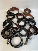 Top view of 13 assorted leather belts, mixed black and brown colors, various styles including braided and smooth finishes, different buckle types.