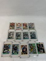 13 assorted NFL football player trading cards in protective cases, front view, showing player images and team logos.