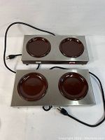 Top view showing two 2-station coffee warmers with brown circular warming plates, stainless steel body, power cords, and on/off switches.