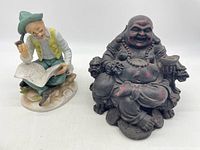 Both figurines together: a colorful old man reading and smoking, and a burgundy Buddha statue seated on a throne.