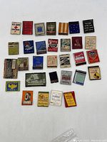 31 assorted vintage collectible advertising matchbook covers and match boxes laid out on flat surface showing different colors, brands and designs