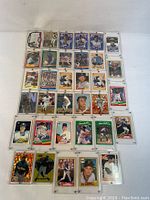 Front view of 34 assorted MLB baseball player collectible trading cards arranged in 5 rows, many in protective plastic sleeves, showing player images and card designs.