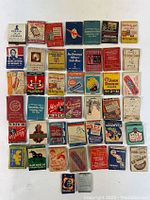Top-down view of 44 vintage advertising matchbook covers and match boxes arranged in rows showing various brands and designs, some showing wear and vintage signs.