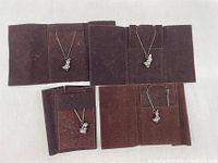 Four sterling silver rabbit/bunny pendants on chains displayed on brown suede-like holders arranged in two rows