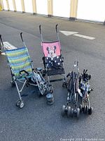Photo showing all five assorted baby strollers arranged outside on asphalt including Minnie Mouse and patterned stroller and three black umbrella strollers folded