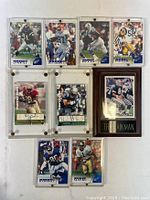 Front view of all 9 football player trading cards arranged in two rows. Each card has player image and autograph under protective plastic casing.