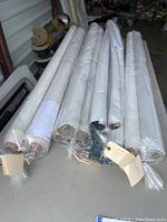 Multiple rolls of automotive vinyl covers in plastic wrapping, mostly white color with one tan visible, laid out on a table.