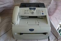 Front angled view of Brother FAX-2820 fax machine with control panel, keypad, handset, and paper output slot visible. Machine is off-white/beige with visible scratches.