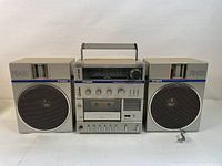 Front view of the vintage Fisher PH-422K boombox with two detachable speakers, cassette player and control panel visible, handle on top, power cord lying beside the right speaker.