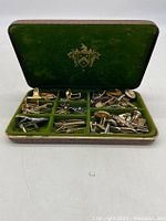 Open jewelry box showing green velvet compartments filled with various cufflinks and tie clips