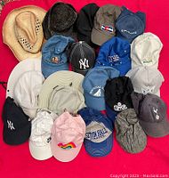 Lot of assorted hats including baseball caps, trucker hats, and sun hats in various colors and styles arranged on red surface.