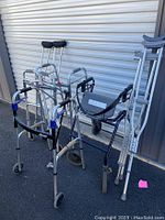 Photo showing assorted walking aids including crutches, multiple walkers and a knee scooter with different designs and sizes.