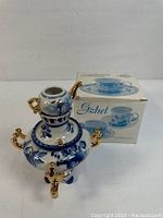 Front and side view of blue and white porcelain samovar with gold accents, with original box in background
