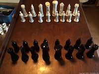 Front-on image of black and white chess pieces arranged in starting position on a wooden surface without a board.
