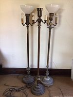 Full view of three tall floor lamps with metal bases, multiple sockets, two with opaque globes and one missing globe.