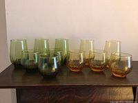 Front view of 10 glasses on a dark wooden surface, 5 green-tinted and 5 amber-tinted, arranged in two rows.