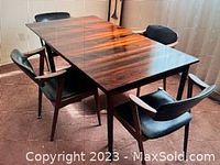 Diagonal view of rectangular wood veneer dining table on carpet with four black upholstered chairs