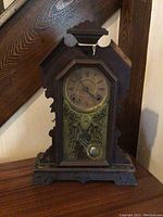 Front view of vintage wooden mantel clock showing full clock body, glass front panel, clock face with Roman numerals, and visible pendulum.