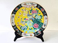 Full view of antique Chinese porcelain charger on wooden display stand showing colorful peacock and floral design with yellow background and decorative border.