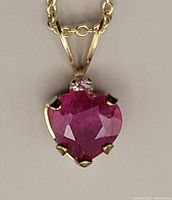Close-up image of the heart-shaped ruby pendant with small diamond on top in 10kt yellow gold setting.