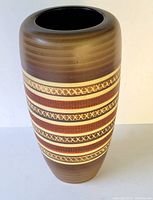 Front angle view of tall brown ceramic vase with horizontal textured bands showing relief design details and color variation.