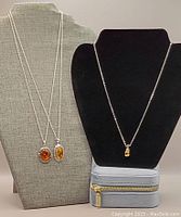Three sterling silver chains displayed on two necklace busts, each holding a pendant with amber or citrine stones. Box visible underneath.