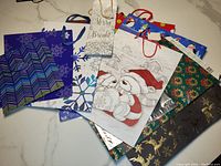 Twelve assorted Christmas gift bags with various holiday designs, overlapping on a flat surface