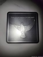 Close-up of the metallic holder featuring an engraved dove design on its lid, showing minor surface scratches.