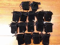 Multiple groups of black felt jewelry bags of two sizes stacked on wooden floor.