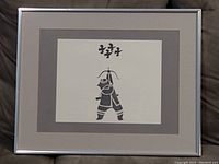 Framed print showing a black silhouette of a samurai warrior holding a spear with gray matting and silver metal frame on a couch background.