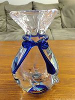 Front and side view of a clear glass vase with blue decorative accents on a wooden surface against a sofa background.