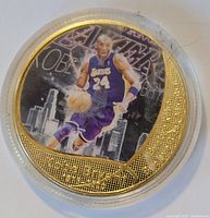 Close-up of front side of gold plated Kobe Bryant coin with color image of the player in Lakers jersey number 24.