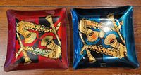 Two hand painted square dishes with musical instrument designs, one red and one blue, on a wooden surface.