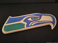 Front side of the wooden sea hawk carving showing blue and green painted design with cream background.