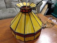 Side view of the stained glass chandelier shade showing yellow glass panels with a red horizontal band around the widest part and metal chain attached.