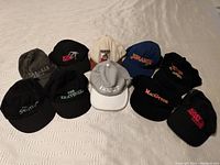Ten assorted movie and Disney themed hats arranged on a light-colored surface showing different colors and logos including Jumanji and MacGyver