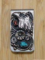 Front view of the nickel/silver money clip showcasing eagle head relief with red and turquoise stone inlays and decorative floral details
