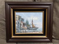 Full view of framed oil painting showing coastal village and sailboat on water.