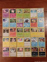 Full view of 30 Pokémon cards arranged flat on wooden surface showing front artwork of each card.