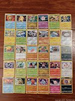 Full view of 30 assorted Pokémon cards arranged in rows on wooden table showing various Pokémon characters and card details.
