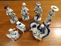 Wide view of the seven porcelain figures in the lot arranged on a wooden table.
